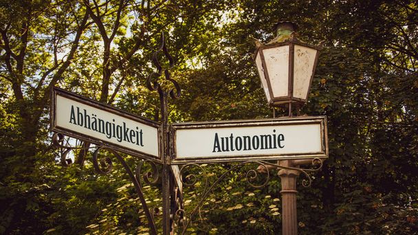 Una imagen con una señal apuntando en dos direcciones diferentes en alemán. Una dirección apunta a la autonomía, la otra apunta a la dependencia. - Foto, Imagen