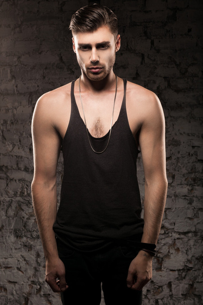Handsome muscular man in a black t-shirt standing near the wall - Photo, Image