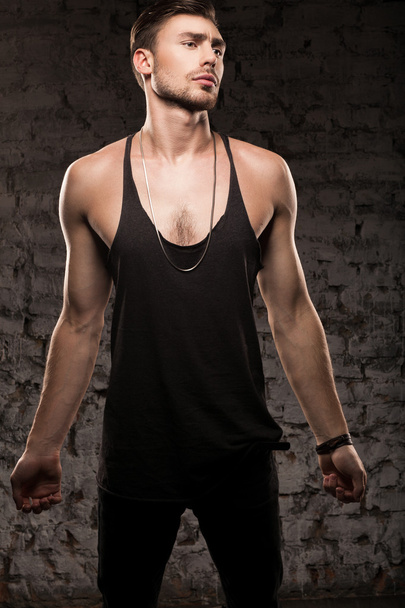 Hombre musculoso guapo en una camiseta negra de pie cerca de la pared
 - Foto, Imagen