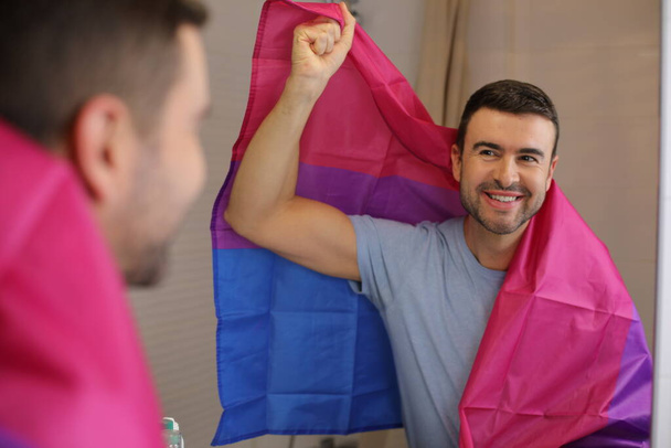 Banyoda aynanın önünde Biseksüel Bayrağı olan yakışıklı bir gencin portresi. - Fotoğraf, Görsel