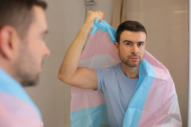 retrato de joven guapo con bandera transgénero delante del espejo en el baño - Foto, imagen