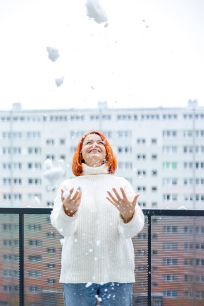 gelukkig jong vrouw met rood haar staan onder de sneeuw op het balkon en gelukkig lachen - Foto, afbeelding