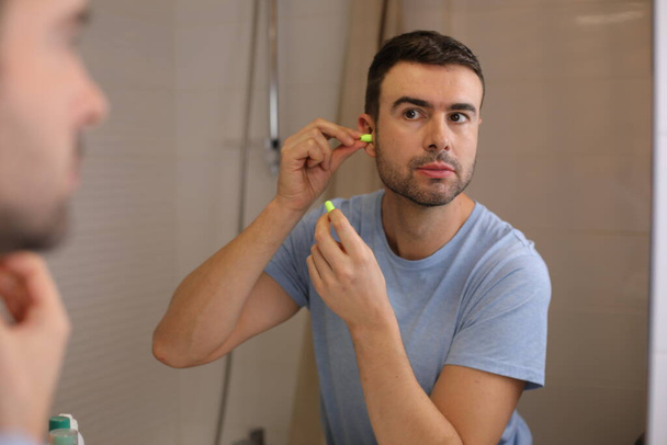 portrét pohledného mladého muže s ucpávkami do uší před zrcadlem v koupelně - Fotografie, Obrázek