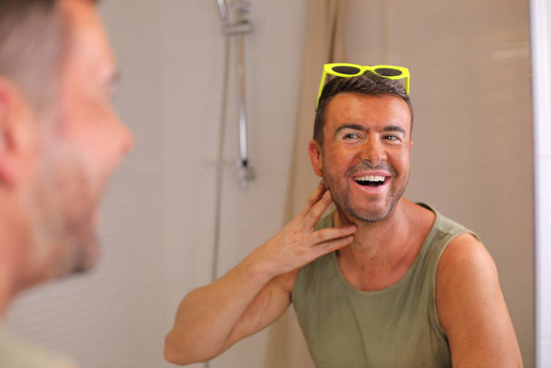 Porträt eines hübschen jungen Mannes mit Sonnenbrand vor dem Spiegel im Badezimmer - Foto, Bild