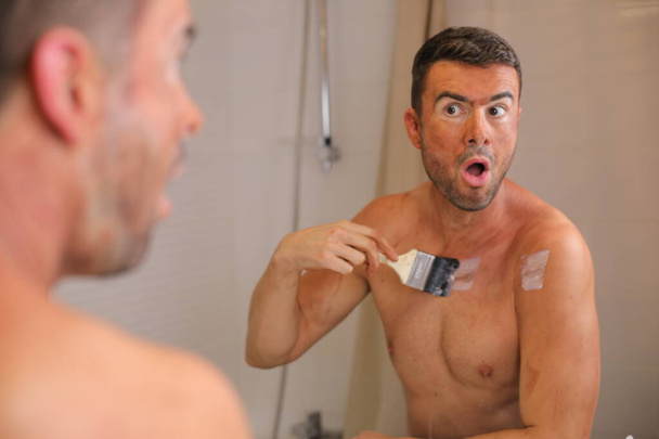 портрет красивого молодого человека с бронзером на коже перед зеркалом в ванной комнате - Фото, изображение