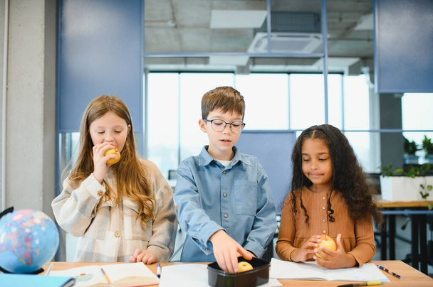 Multiracial schoolchildren having lunch at the desk during a break in school. - Fotó, kép