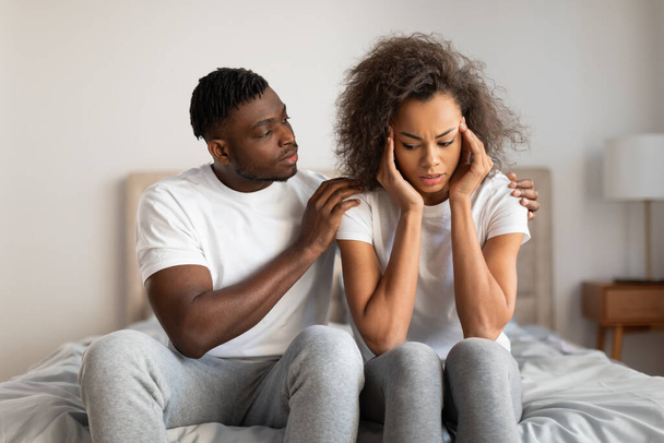 Внимательный молодой чернокожий муж утешает свою расстроенную жену, трогает ее за плечи и говорит слова поддержки, сидя вместе в спальне, справляясь с проблемами. Поддержка и доверие между партнерами - Фото, изображение