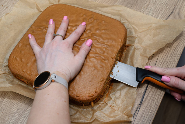 Preparación de pastel polaco, caramelo con crema de crema, mujer corta el pastel en dos partes. - Foto, imagen