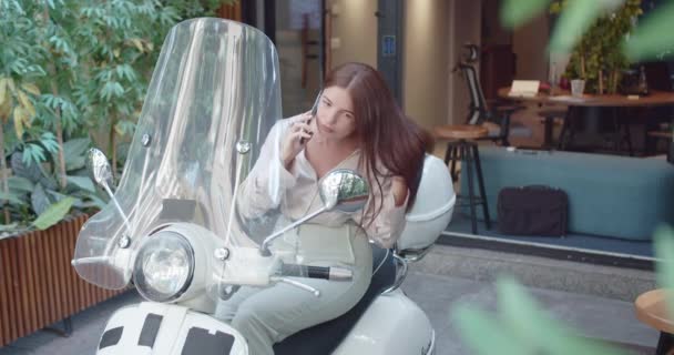 Krásná žena sedí na motorce mluvit s klientem na telefonu, zatímco se dívá na sebe . - Záběry, video