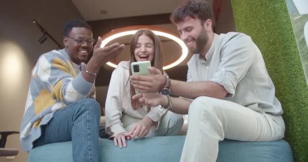 Za třetí, multiraciální spolupracovníci sedící na gauči na prahu a sledující vtipná videa na chytrém telefonu, zatímco si dávají pauzu od práce. Užívají si bytí a spolupráci v pozitivní atmosféře. - Záběry, video