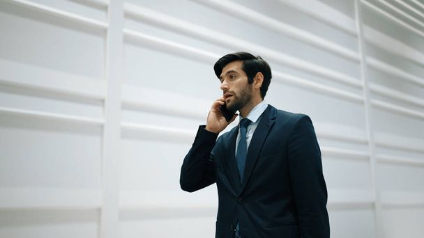 Skilled manager using phone call to contact colleague about project. Handsome male leader calling his business team to report and discuss about sales while standing at white background. Exultant. - Photo, Image