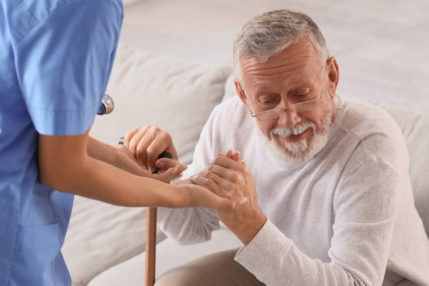 Nurse helping senior man with stick to stand up at home - Photo, Image