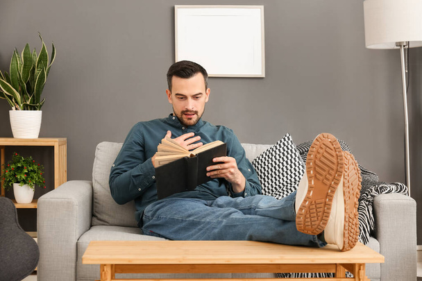 όμορφος άνδρας διαβάζοντας το βιβλίο στον καναπέ στο σπίτι - Φωτογραφία, εικόνα