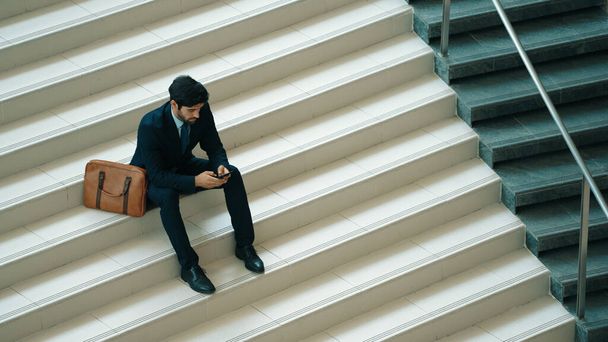 Бізнесмен сидить на сходах, використовуючи бізнес-стратегію мобільного телефону. Кваліфікований менеджер проектів, який працює, використовуючи смартфон контактної бізнес-команди або інвестора під час носіння костюму. Досвідчений. - Фото, зображення