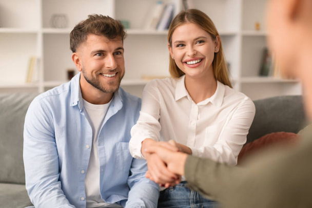 Couples therapy. Grateful husband and wife shaking hands with their therapist at psychologists office, marking successful resolution to their marital issues during a counseling session - Photo, Image