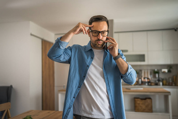 One man adult caucasian male use mobile phone smartphone to make a call talk at home wear shirt and eyeglasses real person copy space - Photo, Image