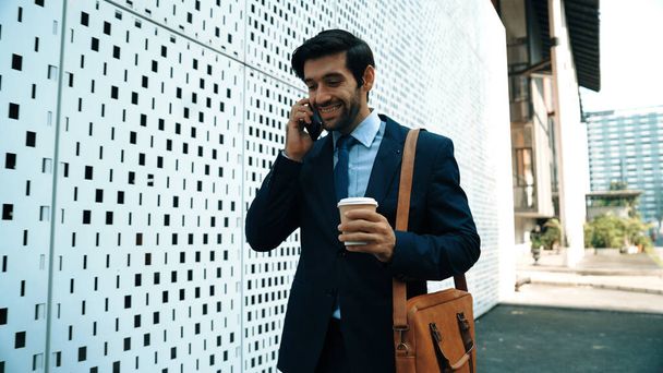 Έξυπνος επιχειρηματίας που χρησιμοποιεί το τηλέφωνο για να μιλήσει για επιχειρηματικές επενδύσεις. Ευτυχής διαχειριστής περπάτημα στο δρόμο, ενώ μιλάμε για έξυπνο τηλέφωνο για να συζητήσουν επιχειρηματικό σχέδιο ή στρατηγική μάρκετινγκ ή εργασίας. Διεγερτικό. - Φωτογραφία, εικόνα