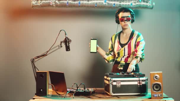 DJ artista muestra plantilla de pantalla verde, mientras que ella utiliza tocadiscos teclas de control para el ajuste de graves, la creación de música techno moderna en la fiesta de discoteca. Mujer músico con cromakey plantilla. - Metraje, vídeo