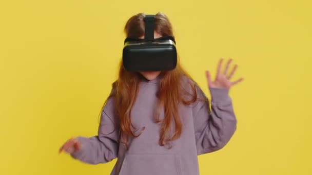Возбужденный счастливый ребенок девочка-подросток, использующий гарнитуру шлем приложение для игры моделирования. Просмотр видео виртуальной реальности 3D 360. Дети в защитных очках изолированы на жёлтом фоне. Технологии будущего - Кадры, видео
