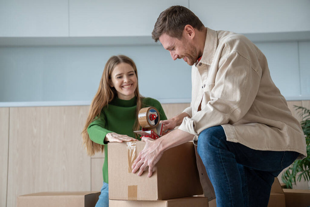 Šťastný pár manželé muž a žena balení lepenkové krabice společně pohybující se v novém bytě. Usmívající se manžel se chystá přestěhovat do jiného domu. Přemístění, koncept rodinné hypotéky. - Fotografie, Obrázek