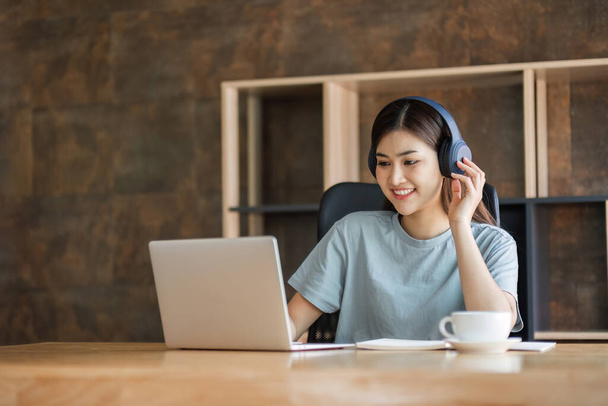 Mladá studentka nosí sluchátka sedí soustředěně a šťastně studuje on-line na svém notebooku v obývacím pokoji doma.. - Fotografie, Obrázek
