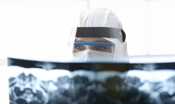 Docteur en costume anti-peste protecteur regardant les rayons X. Diagnostic de la pneumonie covide concept - Photo, image
