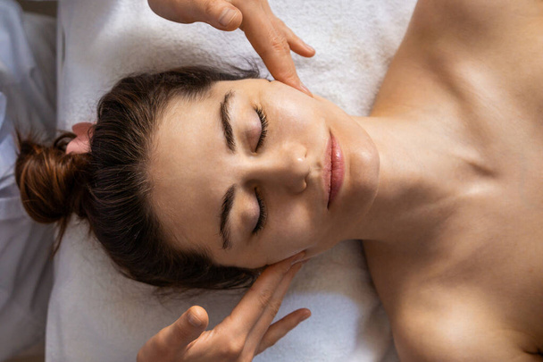 Кавказька жінка отримує масаж обличчя в естетичному салоні. Концепція краси тіла та обличчя. - Фото, зображення