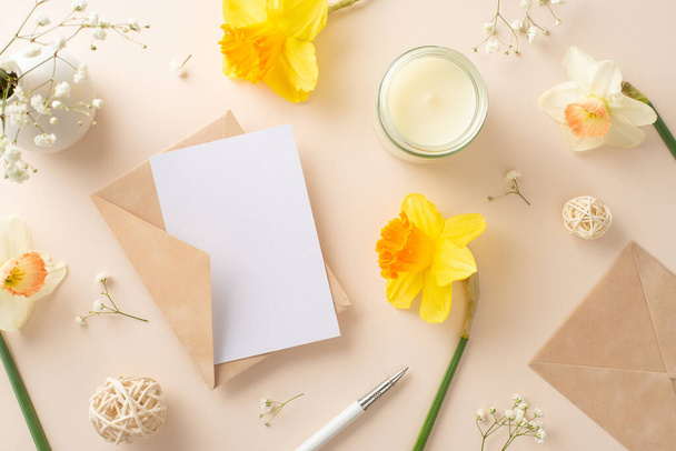 Embrace the joy of spring celebrations with daffodils and gypsophila. Above view photo features flowers, an envelope, and empty paper sheet on a beige isolated backdrop, ideal for adverts or text - Photo, Image