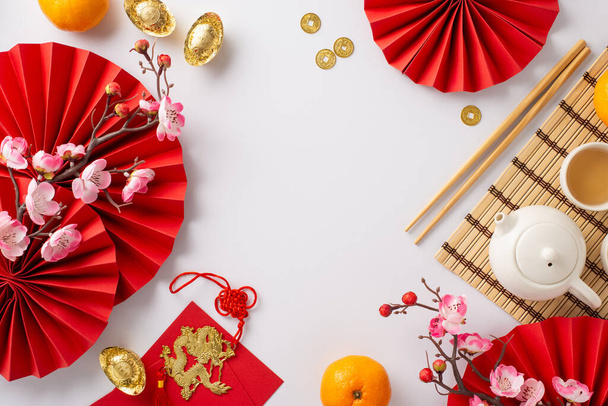 Lunar New Year Dining Setup: Top view fanit, teekutsut asetettu, kolikot, sycee, onnekas punainen kirjekuoret, lohikäärme viehätys sisustus, hedelmät, sakura valkoisella taustalla. Mainosta tämän elinvoimaisen juhlallisen koostumuksen kanssa - Valokuva, kuva