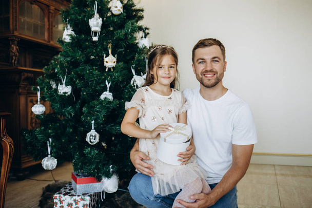 Familia decorando un árbol de Navidad. Joven con su hija sobre sus hombros ayudándola a decorar el árbol de Navidad. - Foto, imagen