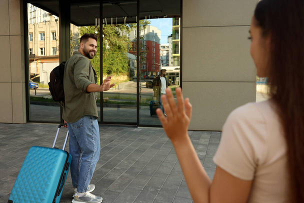 Long-distance relationship. Woman waving to her boyfriend with luggage outdoors, selective focus - Photo, image