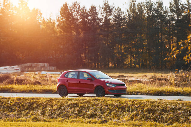 Car speeding in the countryside. Driving fast on a road surrounded by greenery in a modern hatchback. Side view of modern hatchback moving on the highway. - Photo, Image