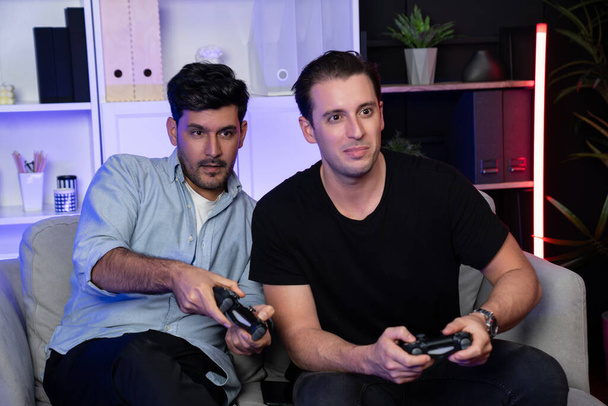 Νικητές και ηττημένοι παίκτες φίλων gamers που παίζουν βιντεοπαιχνίδια στην τηλεόραση χρησιμοποιώντας joysticks στο στούντιο με νέον μπλε φως. Comfy ζουν σε εσωτερικούς χώρους στο σπίτι με χαρούμενα νικητής αγωνίζονται. Πωλητέα. - Φωτογραφία, εικόνα