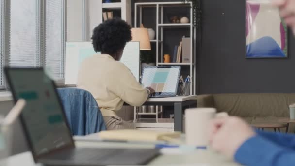 ワイヤレスヘッドフォンでラップトップコンピュータで座って,オフィスのアフリカ系アメリカ人女性同僚と仕事をしている間,コピーブックでメモを取る車椅子の若い白人男性のメディアクローズアップ - 映像、動画