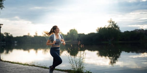 Μια γυναίκα που τρέχει στο πάρκο στο ρεπό της. Αθλητικό μοντέλο φυσικής κατάστασης της ασιατικής εθνικότητας κατάρτισης υπαίθρια για μαραθώνιο. - Φωτογραφία, εικόνα