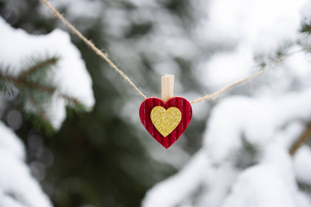 Enfeite de Natal vermelho em forma de coração pendurado em corda de cordel de juta no fundo de abeto coberto de neve ao ar livre. Conceito de amor, família, apoio - Foto, Imagem