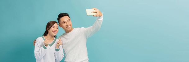 Sonriendo pareja asiática se divierten juntos mientras hacen selfie en el teléfono inteligente sobre fondo azul - Foto, imagen