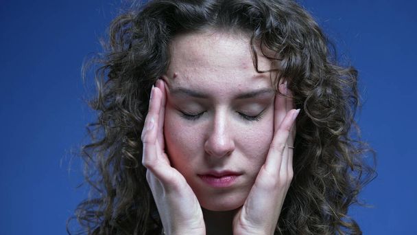 Поддавшись стрессу, молодая женщина пытается успокоить свою нервозность, положив руки на виски головы, чувствуя разочарование и тревогу. - Фото, изображение