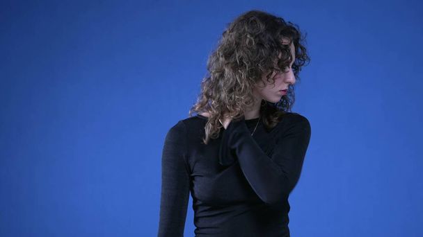 Stressaantunut nuori nainen hankaus kaula yrittää rauhoittaa henkistä ahdistusta seisoessaan sinisellä taustalla - Valokuva, kuva