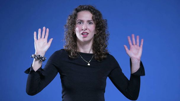Kobieta gestykulująca do kamery rękami sygnalizującymi "cześć" nerwowym językiem ciała. Osoba machająca do oglądającego, nieśmiała ekspresja - Zdjęcie, obraz