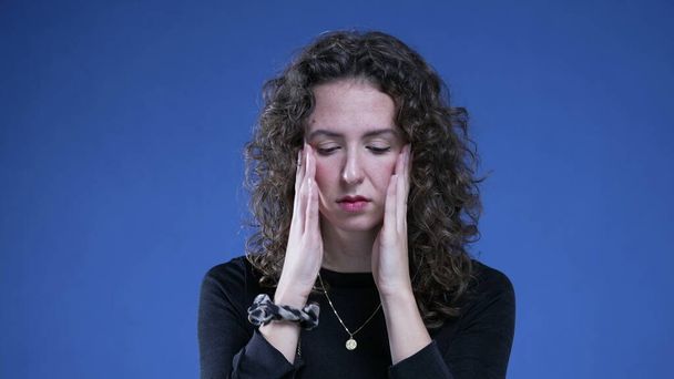 Utanç ve pişmanlık duyan bir kadın mavi arka planda duran endişeli bir ifadeyle yüzünü kapatıyor. 20 'li yaşlardaki insanlar korku ve umutsuzlukla boğuşuyor. - Fotoğraf, Görsel