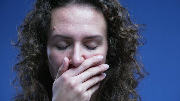 Vyděšená žena reaguje šokovaně a nevěřícně tak, že zakrývá ústa pocitem stresu a předokupace, dívá se přímo na kameru s modrým pozadím. Detailní záběr tvář 20s osoba - Fotografie, Obrázek