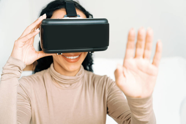 Jonge vrouw die virtual reality VR-bril thuis gebruikt voor cruciale online winkelervaring. De virtual reality VR innovatie geoptimaliseerd voor vrouwelijke digitale entertainment lifestyle. - Foto, afbeelding