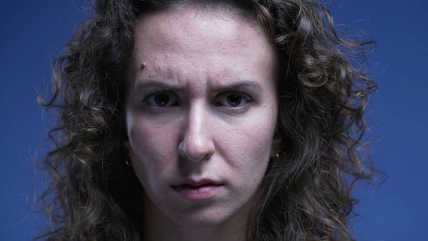 Zaklatott nő ráncolja szemöldök komoly arckifejezéssel egyenesen a kamerába - Fotó, kép