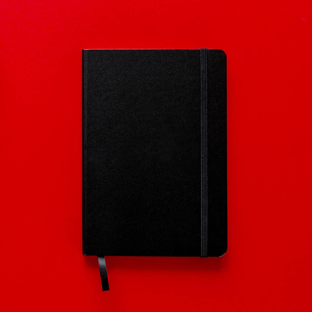Μαύρο σημειωματάριο με σελιδοδείκτη σε κόκκινο φόντο. πάνω όψη - Φωτογραφία, εικόνα