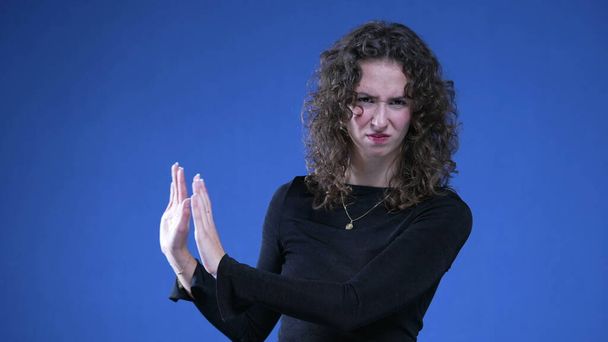 ハンドジェスチャーで拒絶と不信感を表現する20代女性,青い背景に手のひらで押し飛ばす女性 - 写真・画像