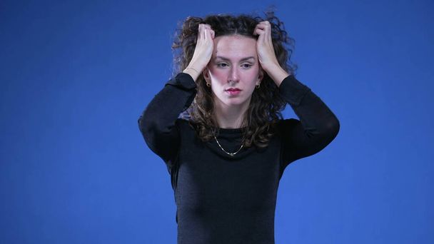 パニックモードで不安な女性は髪を引っ張り,青い背景に立っているボディー言語をこぼします. 困難な時期に夢中になっている絶望的な人 - 写真・画像