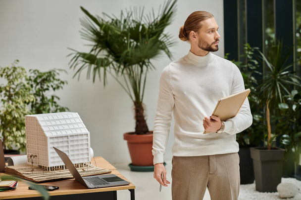 soustředěný atraktivní architekt v bílém pohodlném roláku s plnovousem drží své papíry na startu - Fotografie, Obrázek