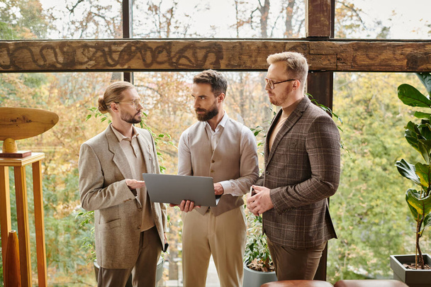 hombres de negocios concentrados de buen aspecto en trajes elegantes discutiendo su proyecto y la celebración de la computadora portátil - Foto, imagen
