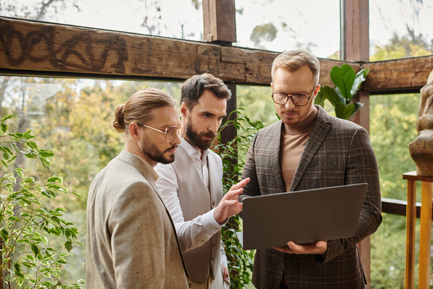 привабливі концентровані бізнесмени в елегантному вбранні обговорюють свій проект і тримають ноутбук - Фото, зображення